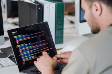 A software developer typing code on a laptop at an office desk