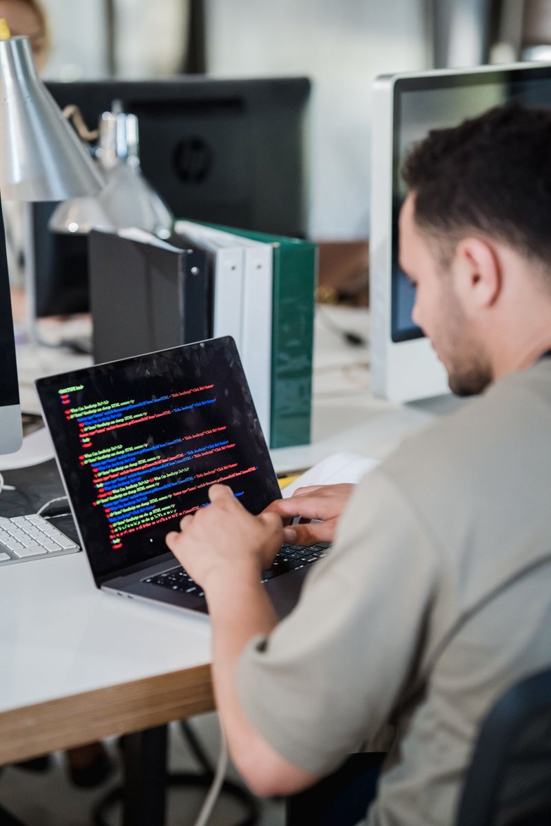 A software developer typing code on a laptop at an office desk