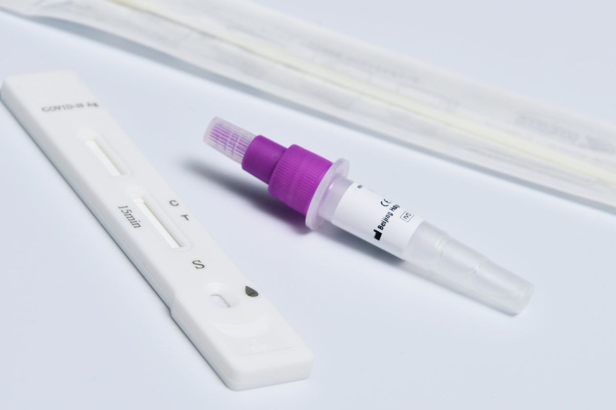 Rapid antigen test cassette beside a purple-capped buffer tube and a sealed sterile swab on a white surface
