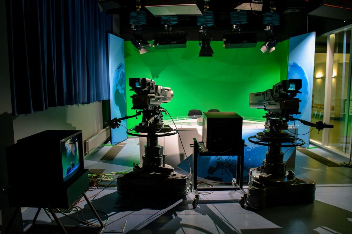 Television studio with professional cameras on pedestals facing a green screen